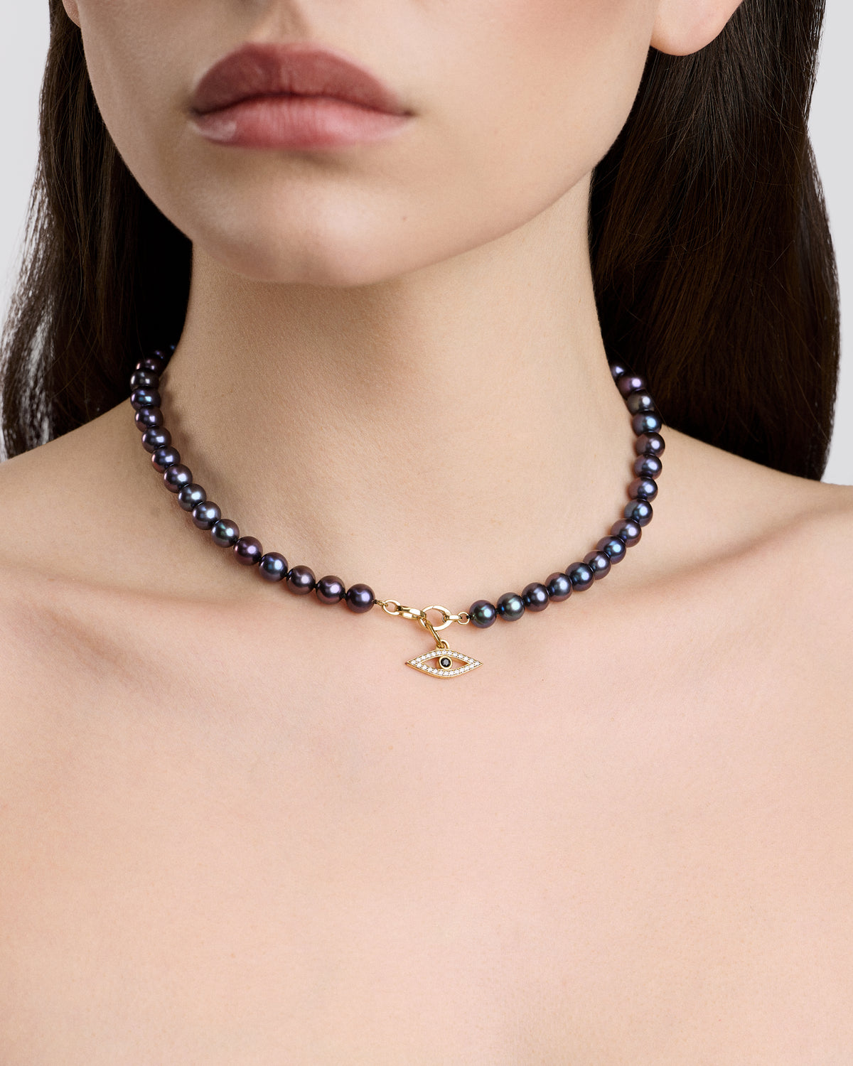 Pearl necklace with a gold evil eye pendant on a model against a neutral background